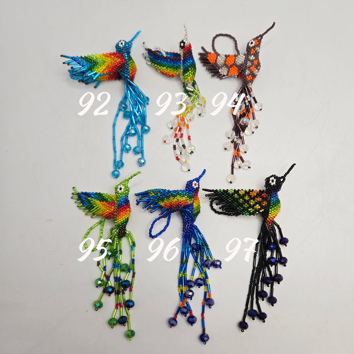 Five handmade beaded hummingbird ornaments displayed on a plain light background, each with a white handwritten number overlay (92 through 97). The birds are crafted from multicolored seed beads with long trailing strands and small bead details.
