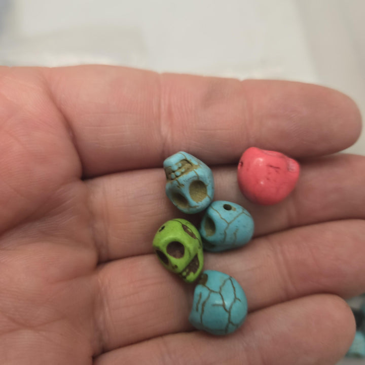 Palm shows four dyed magnesite skull beads in green, blue and coral hues, howlite skull beads style, bulk skull beads