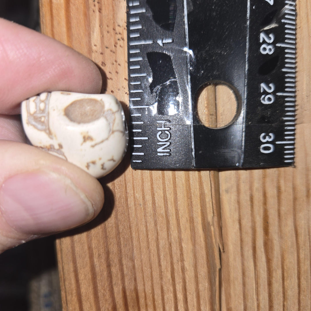 White howlite-style skull bead by ruler showing drilled hole, dyed magnesite beads, bulk skull beads